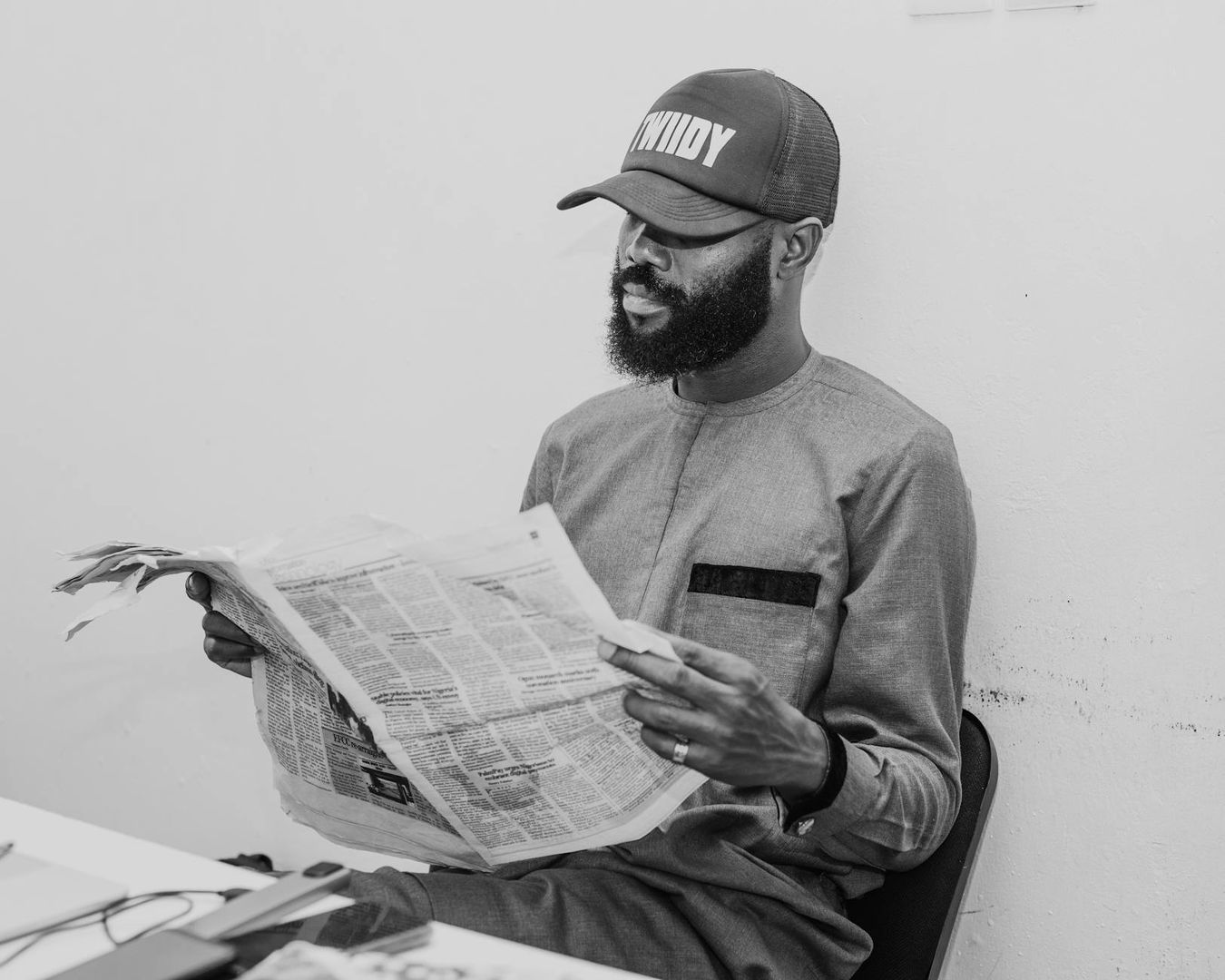 Svartvit bild av en man som läser tidningen med skägg och keps.